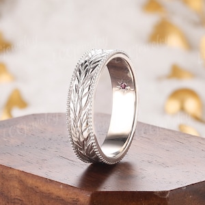 Puede incluir: Una banda de boda de plata con un diseño de hojas y una pequeña piedra roja.
