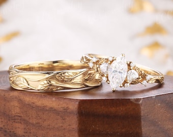 May include: A pair of gold wedding bands with a leaf design. The engagement ring features a marquise-shaped diamond surrounded by smaller diamonds.