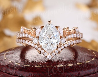 May include: A pear-shaped diamond engagement ring set in rose gold with a delicate leaf design. The ring is set in a box with a red velvet lining.