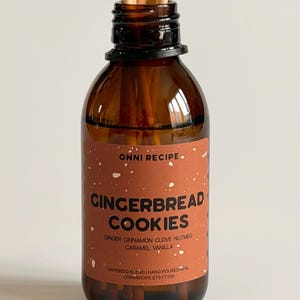 May include: A brown glass aromatherapy diffuser bottle with a label that reads "GINGERBREAD COOKIES." The label lists ingredients: ginger, cinnamon, clove, nutmeg, caramel, and vanilla. The bottle contains a rapeseed blend and has wooden reeds.