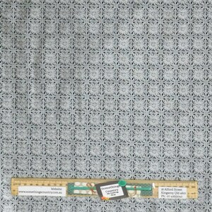 May include: White fabric with a repeating pattern of small, intricate, grey floral designs. The fabric has a subtle sheen and a delicate texture.