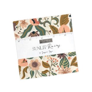 May include: A square stack of fabric squares featuring a floral pattern in shades of cream, peach, dark green, and brown. A white paper band wraps around the centre, printed with "moda FABRICS + SUPPLIES", "SUNLIT Rains", and "BY JESSICA ROJO", with a ruler showing 10 to 20 cm.