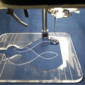 May include: A clear acrylic quilting ruler with printed markings and the text Continuous Figure 8 2.5 and Designed by Leonie West, positioned under a metal sewing machine presser foot with a needle stitching a white thread pattern on blue fabric.