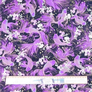 May include: Purple and gold fabric with a repeating pattern of stylised fish with flowing tails and white flowers. The fabric has a glittery finish.