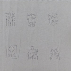 May include: A beige fabric with six embroidered designs. The designs include a flower garden with the text "Smell the flowers", a chicken with the text "Laugh out loud", a heart with the text "Love fiercely", a smiley face with the text "Smile", a fish with the text "Get your feet wet", and a cat.