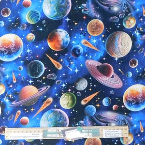 May include: A blue fabric with a repeating pattern of planets, stars and comets. The planets are in various colours, including red, orange, yellow, green, blue and purple. The stars are white and the comets are orange and yellow.