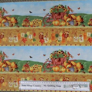 May include: A colorful fabric with a repeating pattern of a red wagon filled with sunflowers, pumpkins, and other fall harvest items. The wagon is on a green hill with a blue sky and white clouds. The fabric has a border of brown leaves and the words "Market" and "Fall" in a banner.