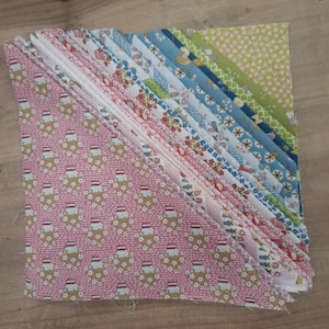 May include: A stack of triangular fabric pieces arranged in a diagonal fan pattern. The fabrics feature various patterns including pink with floral motifs, white with red accents, blue with floral designs, and a green patterned piece at the top corner.