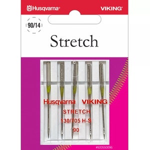 May include: A package of Husqvarna VIKING Stretch sewing machine needles. The package is white and pink with the Husqvarna and Viking logos at the top. The needles are silver with yellow accents. The text "Stretch" is printed on the package.