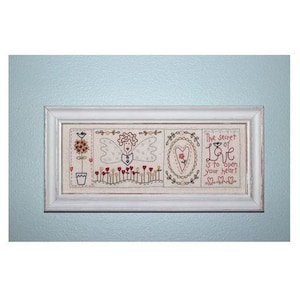 May include: A white framed embroidery with a white background and colourful embroidery depicting a flower, an angel, a heart, and the text "The secret of Love is to open your heart".
