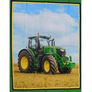May include: A green tractor with a yellow wheel in a field of dry grass under a blue sky with white clouds.
