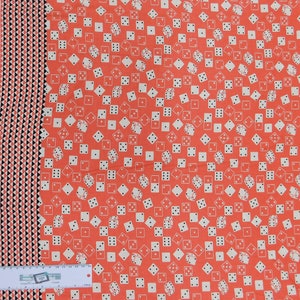 May include: Coral fabric featuring a repeating pattern of white dice. The dice are scattered across the fabric, some showing different sides. A vertical border on the left has a black, white, and coral triangle design. A ruler is at the bottom.