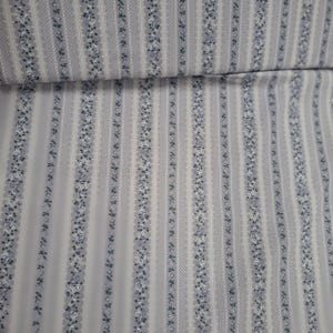 May include: A fabric featuring a repeating vertical pattern of light grey and white stripes. The design alternates between narrow bands of small dark blue floral motifs and wider sections of a fine, intricate white geometric diamond lattice.