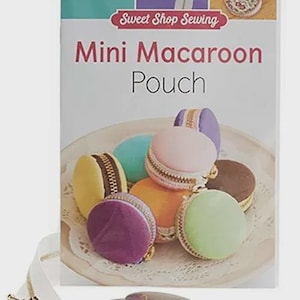 May include: A craft kit for making mini macaron pouches. The kit includes a variety of colorful, zippered pouches resembling macarons, along with a zipper and discs. The packaging reads "Sweet Shop Sewing" and "Mini Macaroon Pouch."