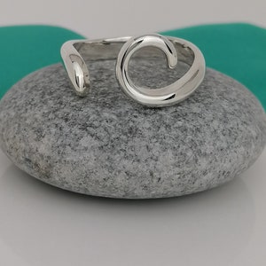 Puede incluir: Un anillo de plata con un diseño de espiral. El anillo está sobre una piedra gris.