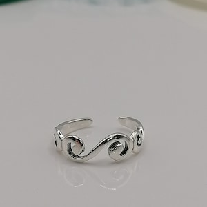Può includere: Un anello per il piede color argento con un design a spirale. L'anello regolabile presenta un design aperto e una finitura lucida. Il design dell'anello è un motivo a onde continuo, che aggiunge un tocco di eleganza al gioiello.