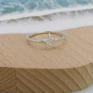May include: A silver ring with a star cut-out design. The ring is on a wooden surface.