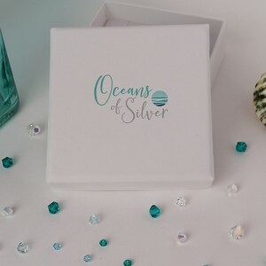 Peut inclure: Une bo&icirc;te blanche avec le logo "Oceans of Silver" imprim&eacute; sur le dessus. Le logo pr&eacute;sente un cercle bleu et vert avec des vagues &agrave; l'int&eacute;rieur.