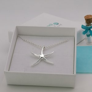 Peut inclure: Un collier en argent avec un pendentif en forme d'&eacute;toile de mer dans une bo&icirc;te blanche. Le collier est dans une bo&icirc;te blanche avec une &eacute;tiquette bleue et blanche qui dit "Seas & Wishes".