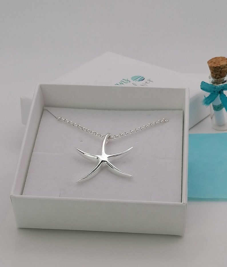 Peut inclure: Un collier en argent avec un pendentif en forme d'&eacute;toile de mer dans une bo&icirc;te blanche. Le collier est dans une bo&icirc;te blanche avec une &eacute;tiquette bleue et blanche qui dit "Seas & Wishes".