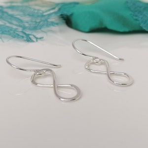 May include: A pair of silver infinity symbol earrings with a simple, delicate design. The earrings are made of thin wire and have a hook fastening.