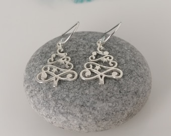 May include: A pair of silver earrings shaped like Christmas trees with a delicate, intricate design. The earrings are on a gray stone.