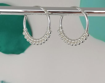 May include: A pair of silver hoop earrings with a beaded design. The earrings are hanging from a silver bar.