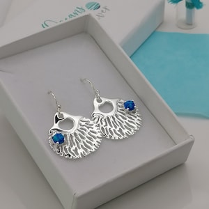 Op de afbeelding: Zilveren oorbellen met een blauwe opaal edelsteen in het midden van elke oorbel. De oorbellen zijn gevormd als een schelp met een getextureerd ontwerp.