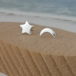 Può includere: Un paio di orecchini d'argento, uno a forma di stella e l'altro a forma di mezzaluna. Gli orecchini sono esposti su una superficie di legno.