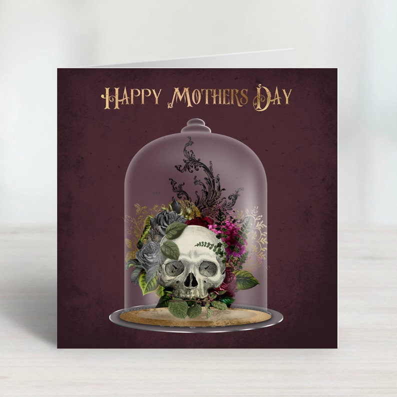 K&ouml;nnte beinhalten: Muttertagskarte mit einem Totenkopf und einem Blumenarrangement unter einer Glasglocke. Die Karte hat einen weinroten Hintergrund mit dem goldenen Schriftzug "Happy Mothers Day".