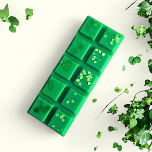 May include: A green wax melt bar with a shamrock design and glitter. The bar is divided into 10 squares.