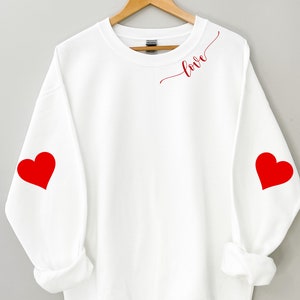 May include: White sweatshirt with red hearts on the sleeves and the word "love" in cursive on the front.