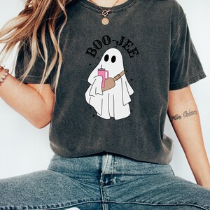 May include: A dark gray t-shirt with a white ghost holding a pink drink and the text "BOO-JEE" in black.