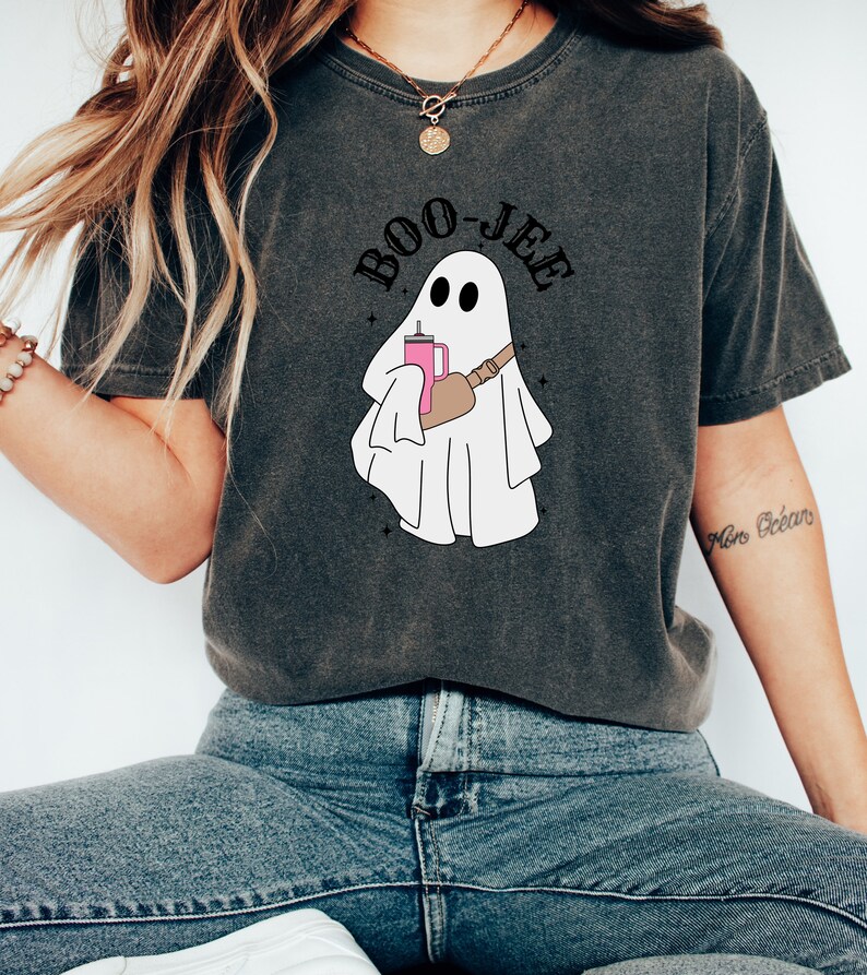 May include: A dark gray t-shirt with a white ghost holding a pink drink and the text "BOO-JEE" in black.