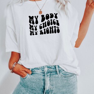 May include: White t-shirt with a black graphic that reads "My Body My Choice My Rights" in a retro font.