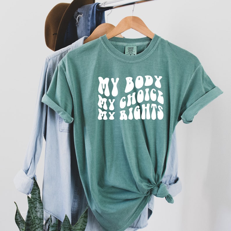 May include: A teal green t-shirt with the text "MY BODY MY CHOICE MY RIGHTS" in white, stylized in a retro font.