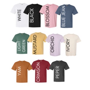 May include: Twelve different color t-shirts with the color name printed vertically on the front of each shirt. The colors are white, black, blossom, blue jean, light green, mustard, orchid, ivory, yam, crimson, pepper.