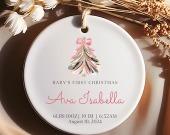 May include: White ceramic ornament with a pink and green watercolor Christmas tree design. The text "BABY'S FIRST CHRISTMAS" is printed in black, followed by the name "Ava Isabella" in pink. The ornament also includes the baby's birth details: "6LBS 10OZ | 19 IM | 6:32AM August 10, 2024".