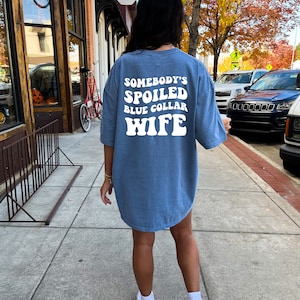 Puede incluir: Una camiseta azul de gran tama&ntilde;o con el texto "Somebody's Spoiled Blue Collar Wife" en blanco.