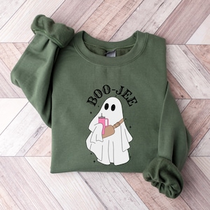 Pu&ograve; includere: Una felpa verde con un fantasma bianco che tiene una bevanda rosa e una borsa marrone. Il testo "BOO-JEE" &egrave; sopra il fantasma.