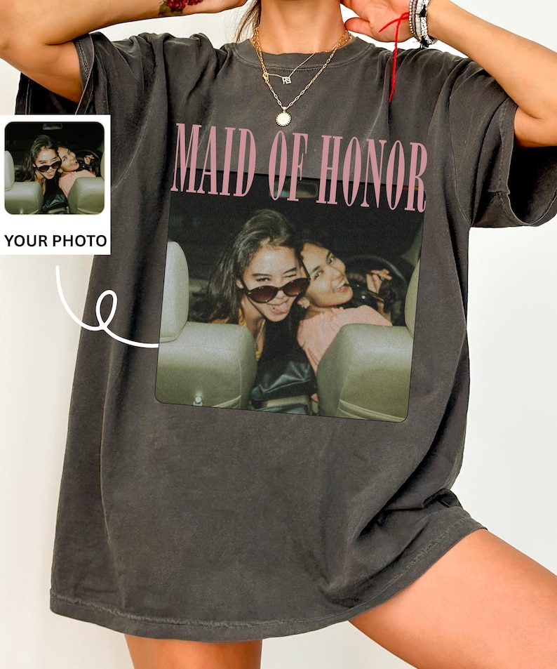 Op de afbeelding: Donkergrijze oversized t-shirt met de tekst "MAID OF HONOR" in roze. De shirt heeft een foto van twee vrouwen in een auto. Een kleinere afbeelding met de tekst "YOUR PHOTO" staat aan de linkerkant van de shirt.