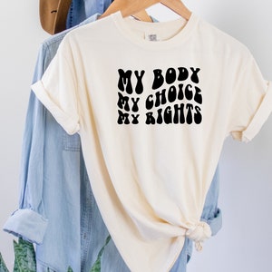 May include: A white t-shirt with black text that reads "MY BODY MY CHOICE MY RIGHTS" in a retro font.