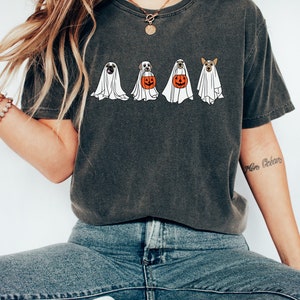 May include: A dark gray t-shirt with a graphic of four dogs dressed as ghosts holding pumpkins. The dogs are a pug, a labrador, a golden retriever, and a corgi.