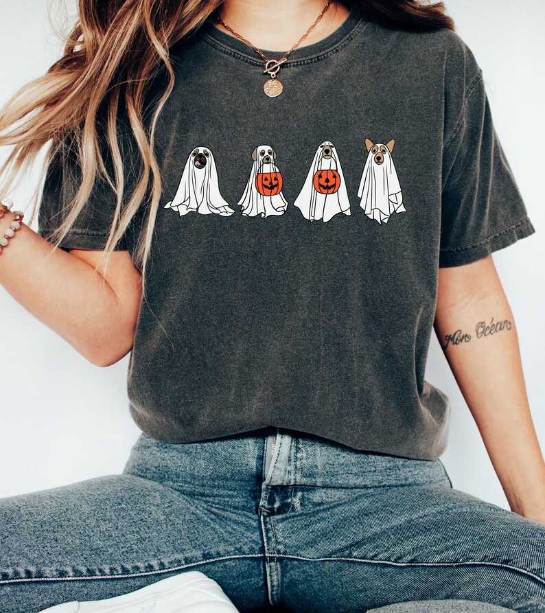 May include: A dark gray t-shirt with a graphic of four dogs dressed as ghosts holding pumpkins. The dogs are a pug, a labrador, a golden retriever, and a corgi.