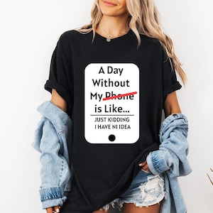 Könnte beinhalten: Ein schwarzes T-Shirt mit kurzen Ärmeln und einer weißen rechteckigen Grafik mit abgerundeten Ecken. Der Text lautet: A Day Without My Phone is Like... JUST KIDDING I HAVE NI IDEA. Eine rote Linie streicht das Wort Phone durch.
