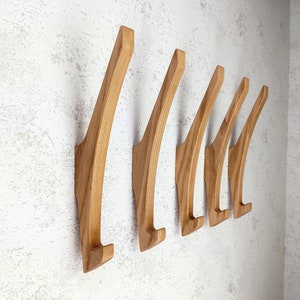 Può includere: Un set di sei ganci da parete in legno con un design curvo. I ganci sono realizzati in legno naturale e hanno una finitura marrone chiaro.