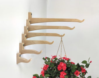 May include: Five wooden wall-mounted plant hangers with a curved design, arranged in a cascading pattern. A hanging planter with red flowers is suspended from the bottom hanger.