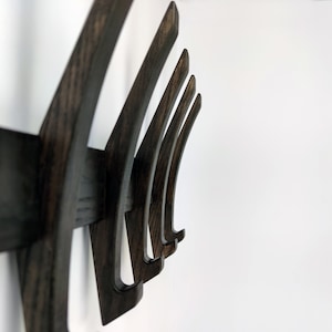 May include: A dark wood wall-mounted coat rack with five curved hooks. The hooks are arranged in a staggered pattern, creating a modern and stylish design.