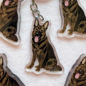 May include: A collection of clear acrylic keychains featuring a printed illustration of a German Shepherd dog sitting with its tongue out. Each keychain is attached to a silver-toned metal split ring by a small chain link, showcasing the dog's black and tan fur pattern.