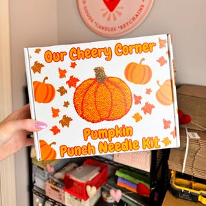 May include: A white box with the text "Our Cheery Corner" and "Pumpkin Punch Needle Kit" on it. The box features a colorful illustration of a pumpkin with fall leaves.